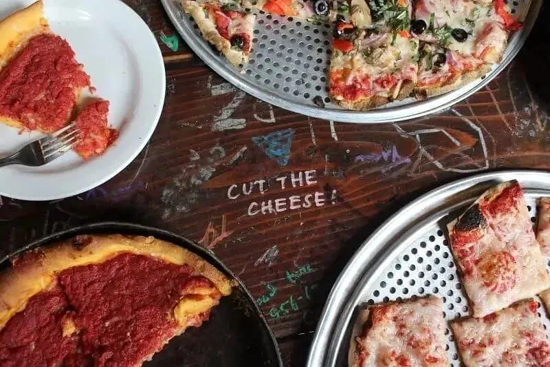 Hands sharing deep-dish pizza topped with vegetables and meat