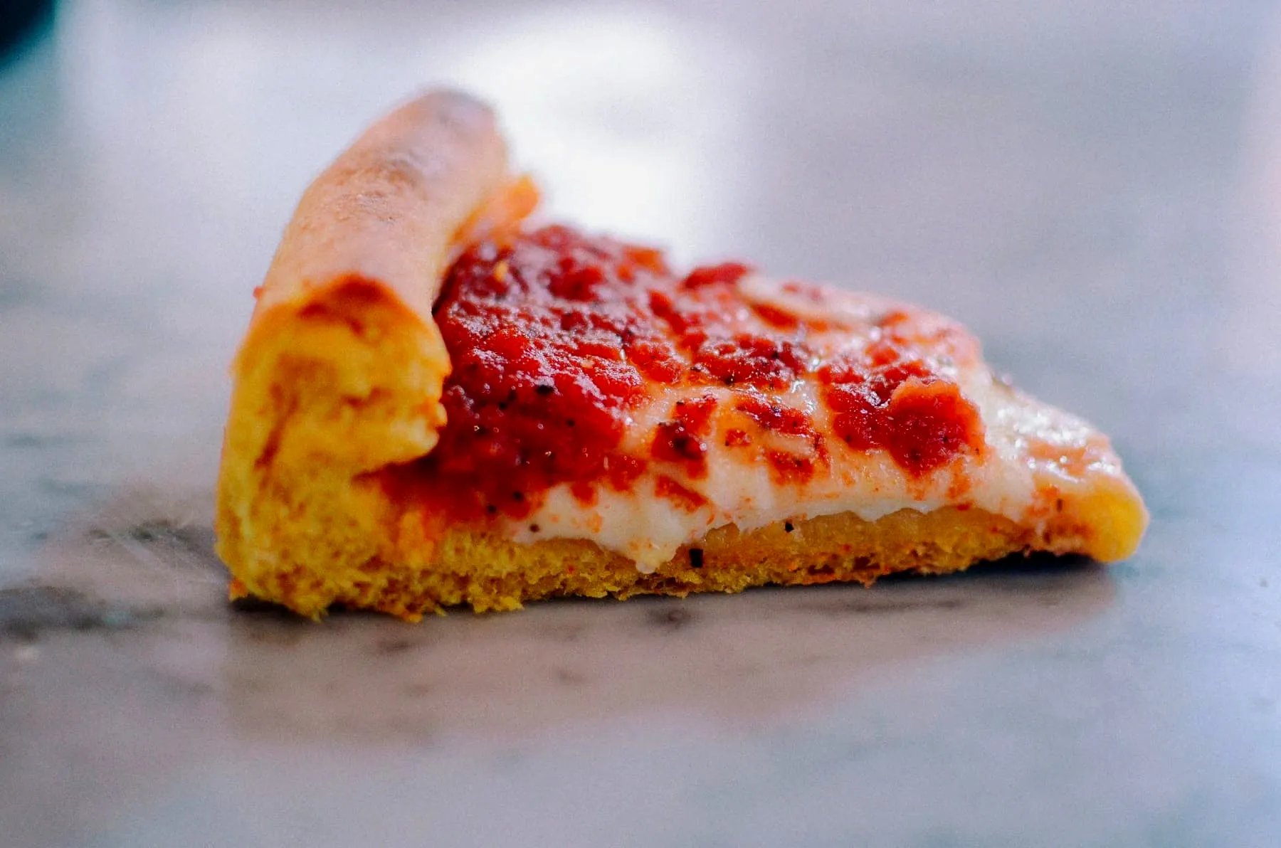 Side view of a single deep dish pizza slice showing its thick sauce and cheese layers