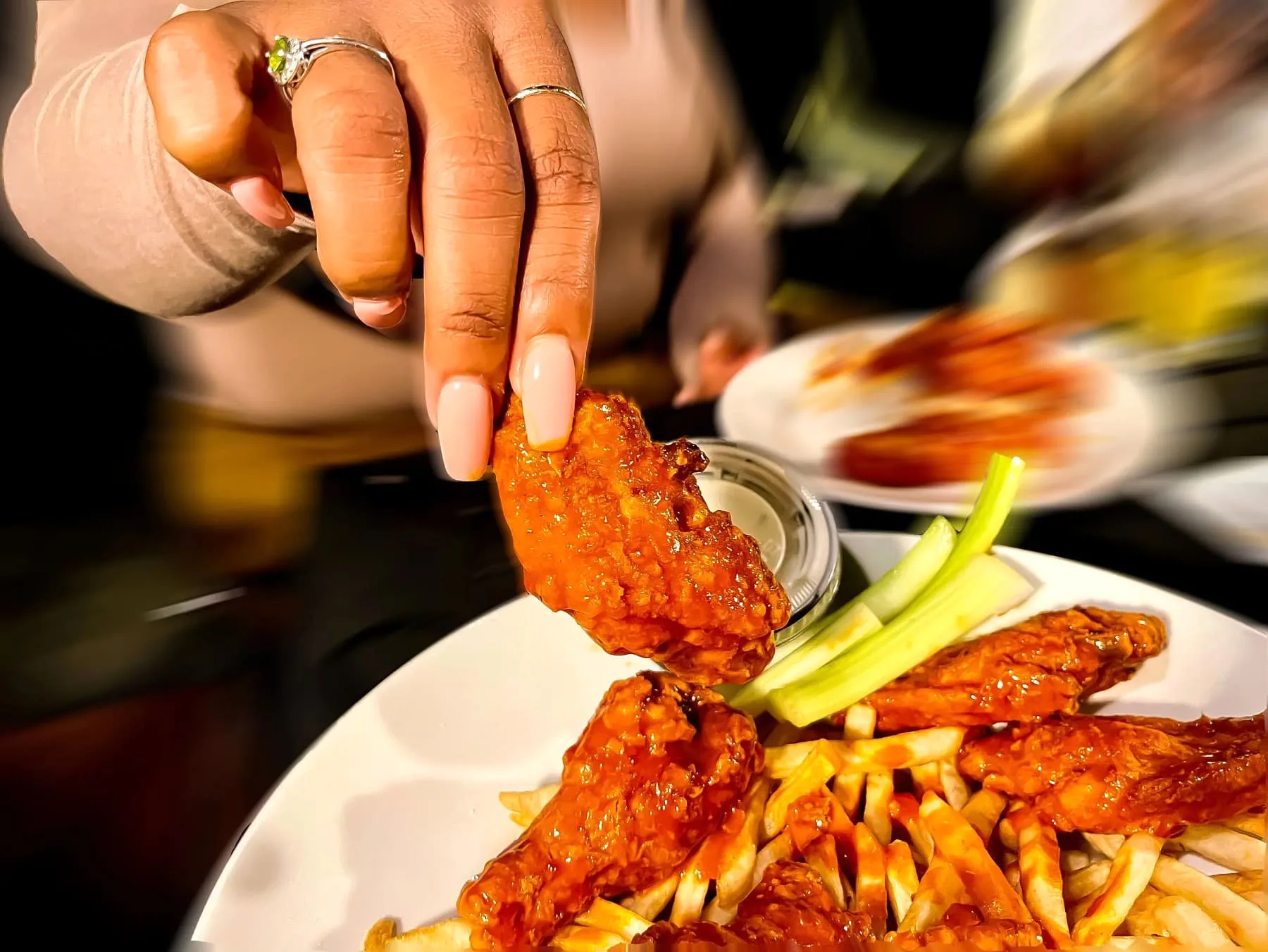 Hand lifting a buffalo wing from a shared catering platter with fries and celery sticks